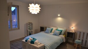 A bedroom with a bed, bedside tables, a nightstand, a lamp, a window, and a radiator. - Chambres Au Pied du Haut Koenigsbourg (Kintzheim)
