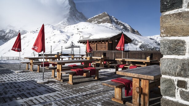 Outdoor wooden benches with red umbrellas, set against a snowy mountain backdrop. - Hotel Schwarzsee (Zermatt)