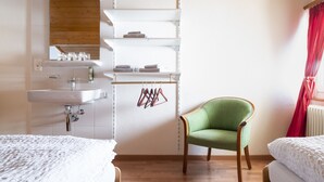 A hotel room with a wooden ceiling, white walls, a green chair, a bed, and a bathroom with a sink and towel rack. - Hotel Schwarzsee (Zermatt)