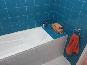 A bathroom with a bathtub, blue tiles, a towel rack with a towel, and a bottle on the counter. - Train station apartment Casa Voyageur (Casablanca)