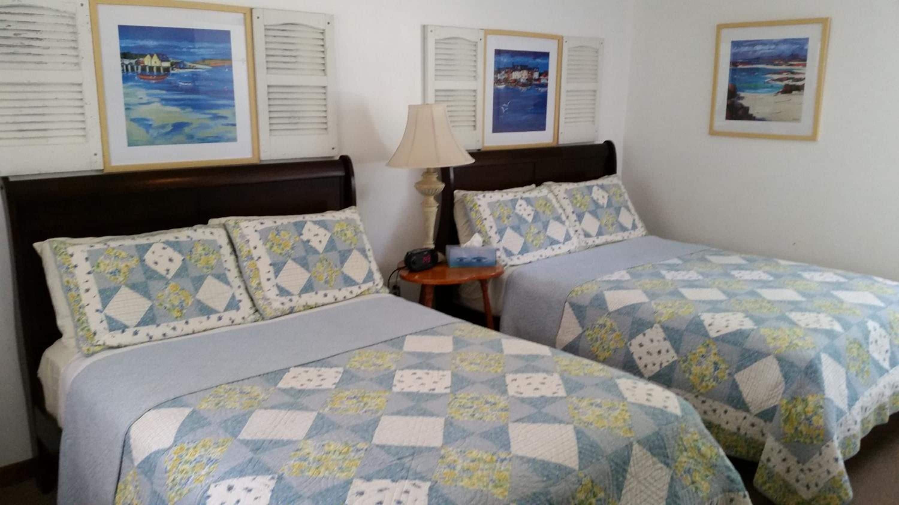 Una habitación de hotel con dos camas, cada una con una colcha estampada, una mesita de noche con lámpara y cuadros en las paredes.