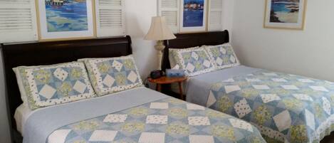 Una habitación de hotel con dos camas, cada una con una colcha estampada, una mesita de noche con lámpara y cuadros en las paredes.