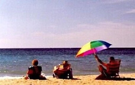 Three people sitting on the beach with a colorful umbrella.