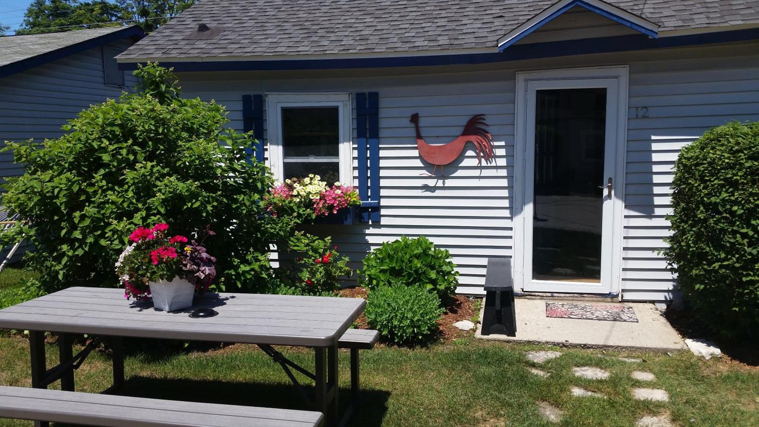 Una casa con fachada azul, una decoración de gallo y una mesa de picnic con flores.