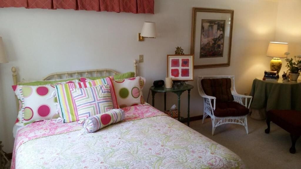 A bedroom with a bed, a chair, a small table, and a lamp.
