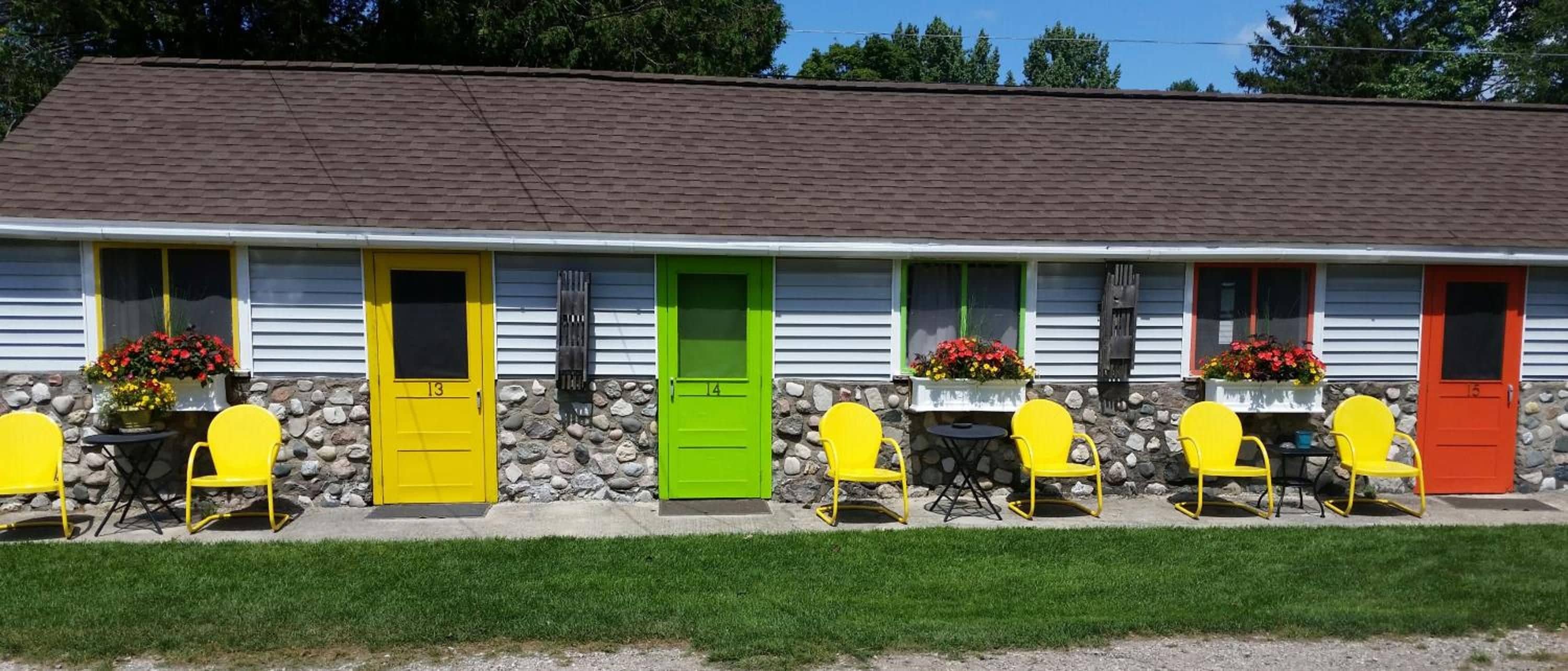 A row of motel rooms with numbered doors, outdoor seating, and flower boxes.