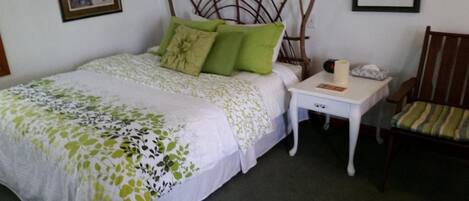 A bedroom with a bed, a nightstand, a chair, and a wall-mounted headboard.