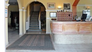 A reception area with a marble counter, a staircase, and a decorative rug. - Hotel Rompeolas (Baiona)
