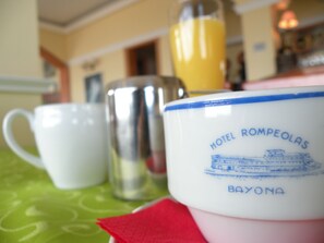 Una mesa con una taza blanca, una taza rosa y un vaso de zumo de naranja.