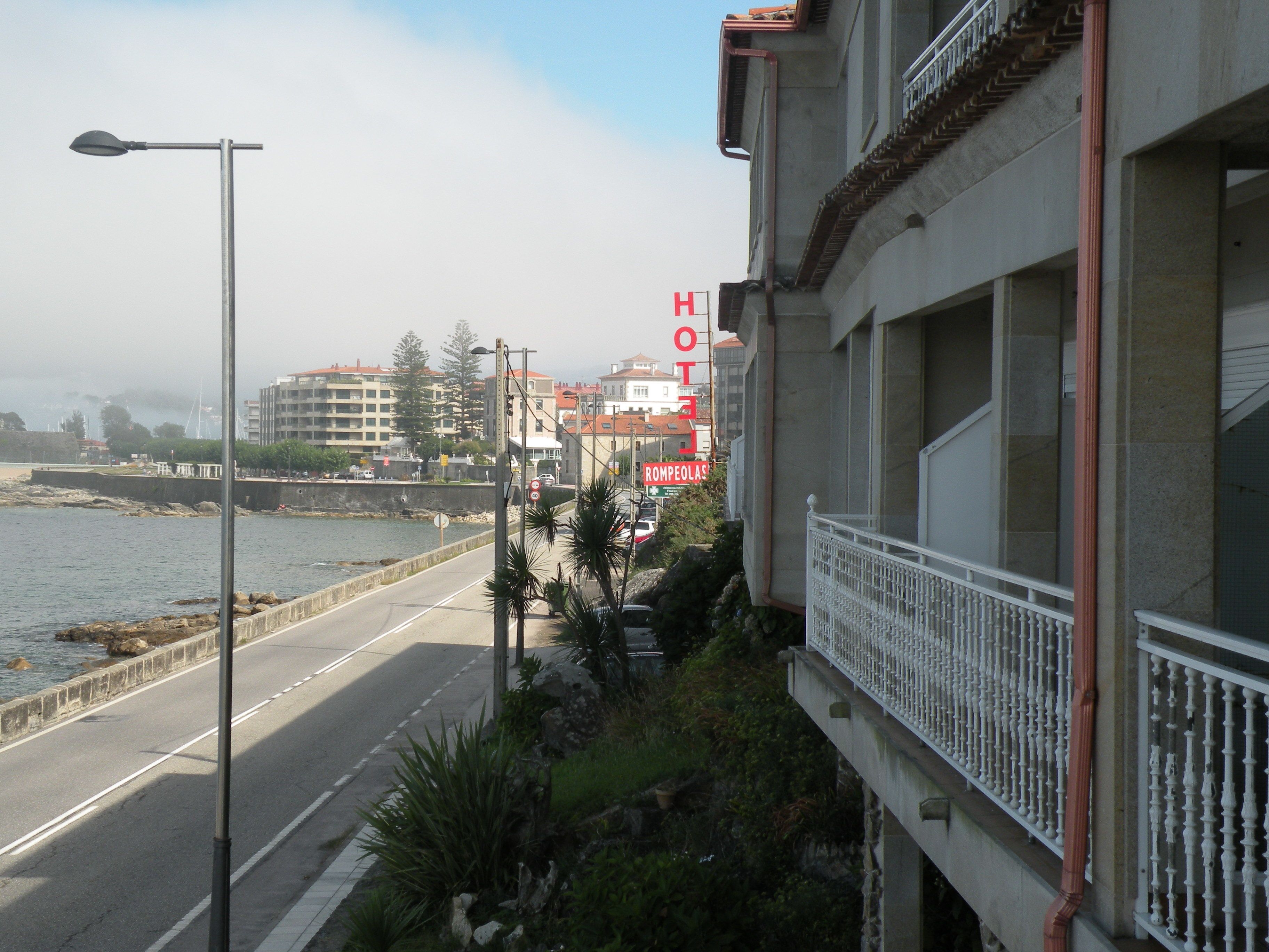 Un hotel frente al mar con balcón y vistas despejadas al camino, y un cartel que indica el nombre y la ubicación del hotel.