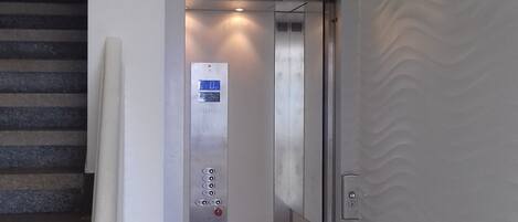 Un ascensor con panel digital, barandilla y pared con textura.
