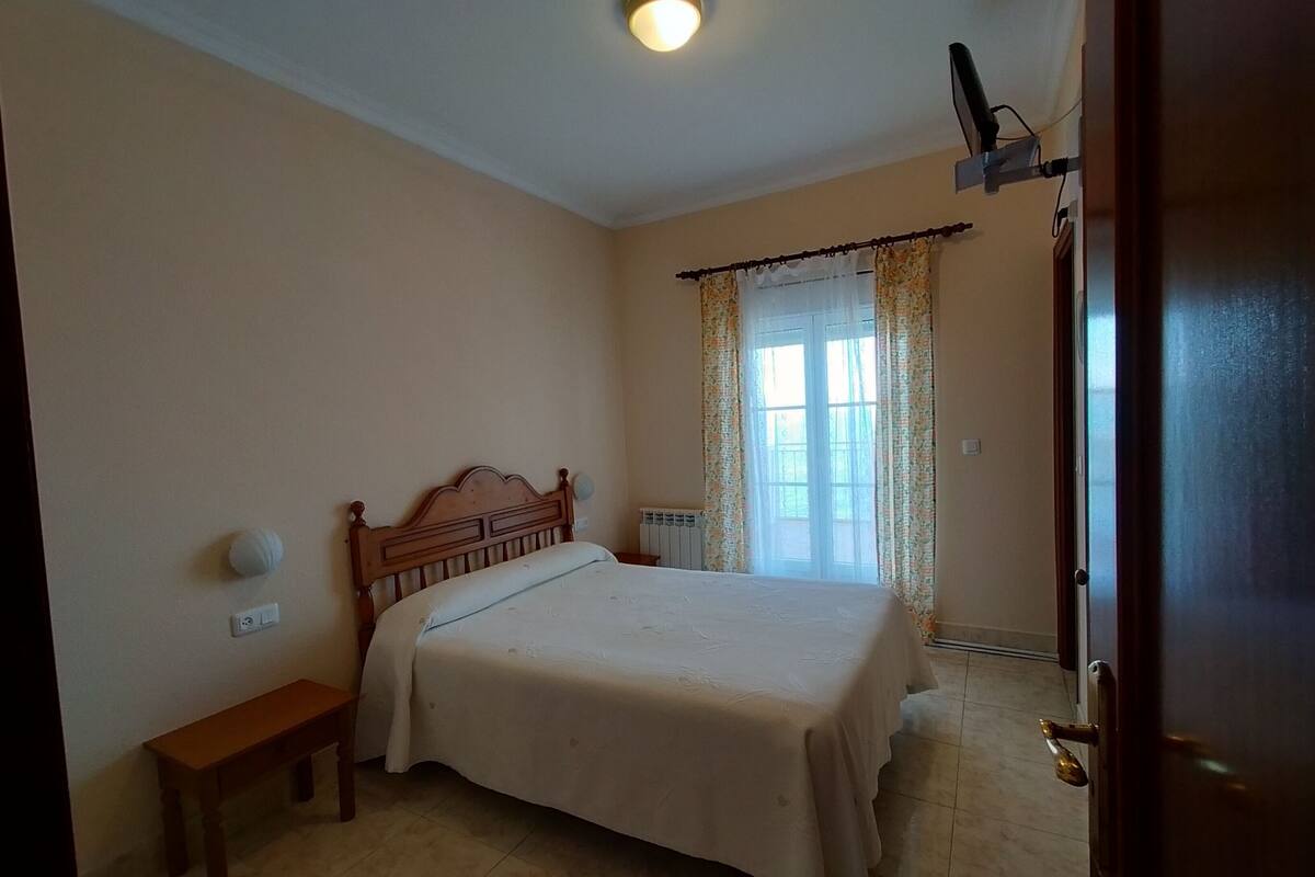 A bedroom with a bed, a bench, a radiator, and a window with curtains.