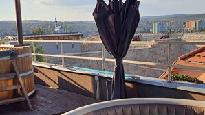 A rooftop terrace with a hot tub, wooden barrels, and a view of a cityscape including a church and residential buildings. - Aparthotel Orient (Eger)