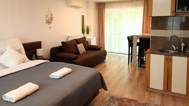A hotel room with a bed, a sofa, a small kitchen area, and a dining table. - Aparthotel Orient (Eger)