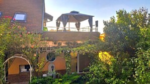 A courtyard with a covered outdoor seating area, a brick building, and lush greenery. - Aparthotel Orient (Eger)