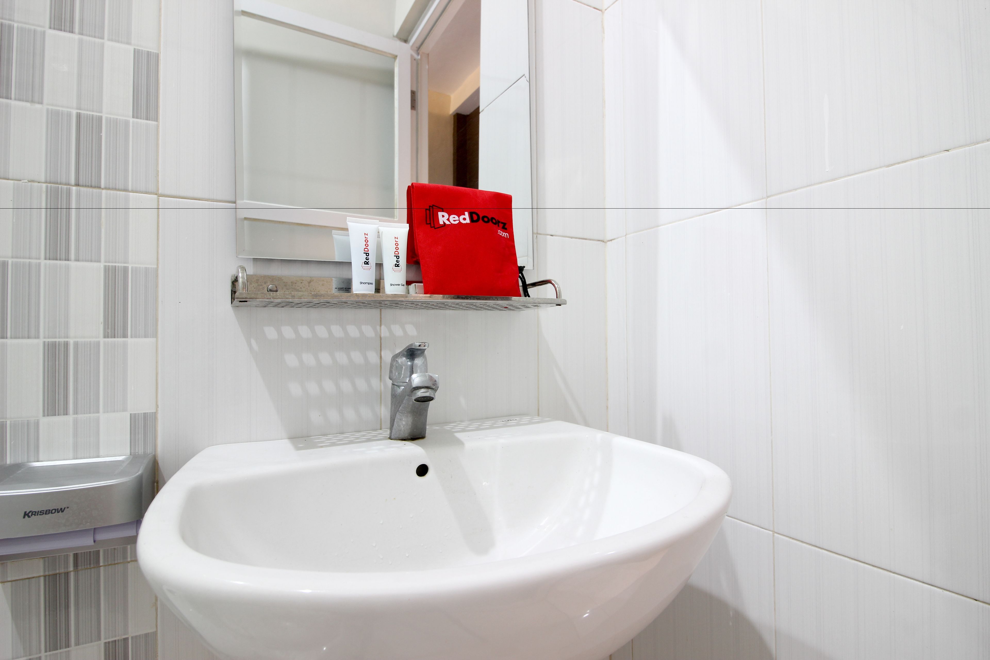 Une salle de bain avec un lavabo blanc, un miroir au-dessus et une étagère où sont présentés des produits RedDoorz.