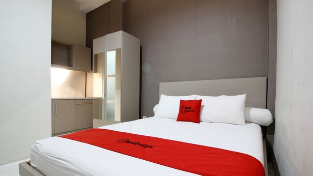Une chambre d’hôtel avec un lit, un plaid rouge, un oreiller blanc orné du texte « Red Doorz » et une armoire.