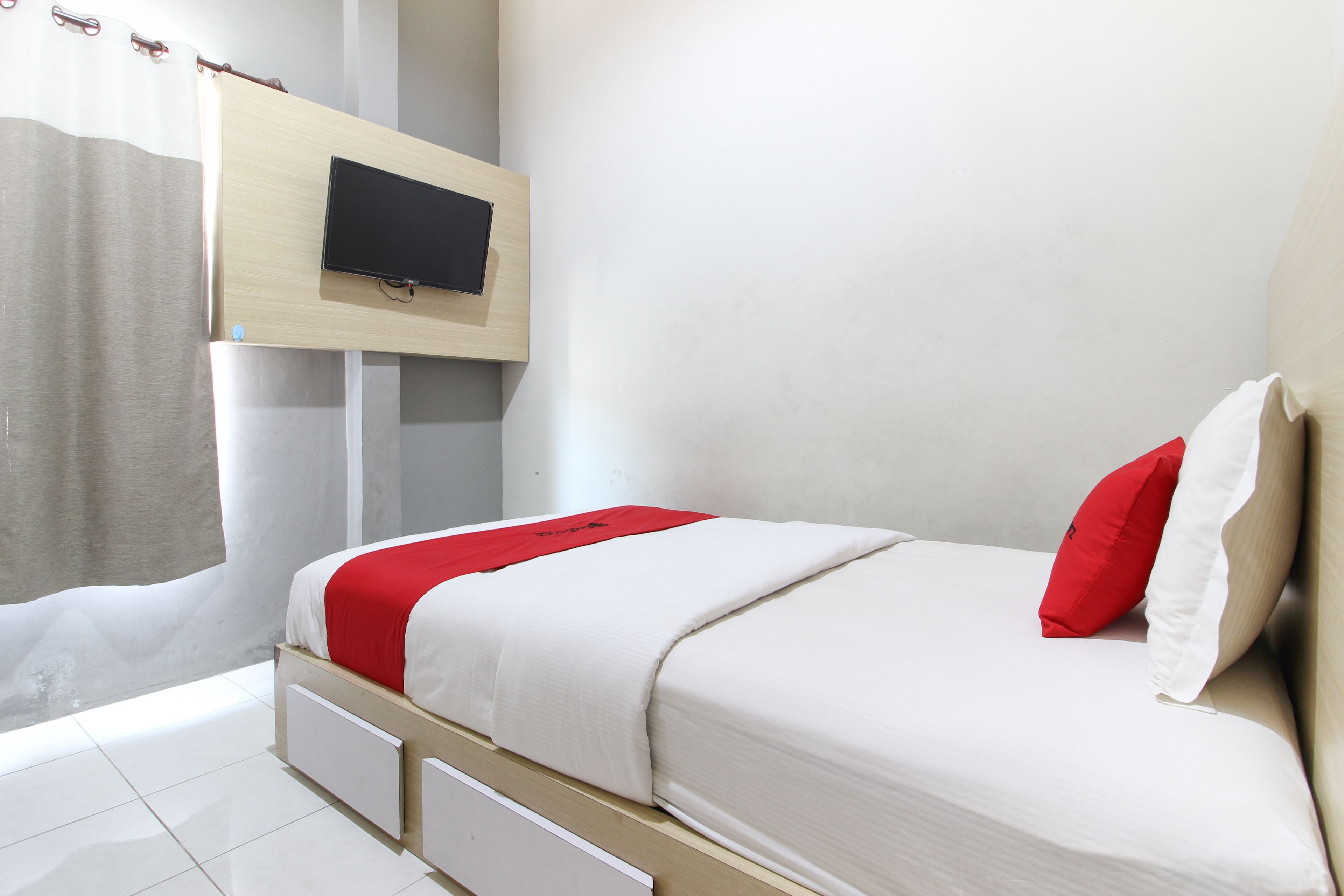 A bedroom with a bed, a TV mounted on the wall, and a window with curtains.