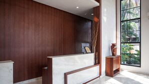 A reception area with a marble counter, wooden panel walls, and a large window with a view of greenery. - RedDoorz Premium @ Raya Nginden (Surabaya)