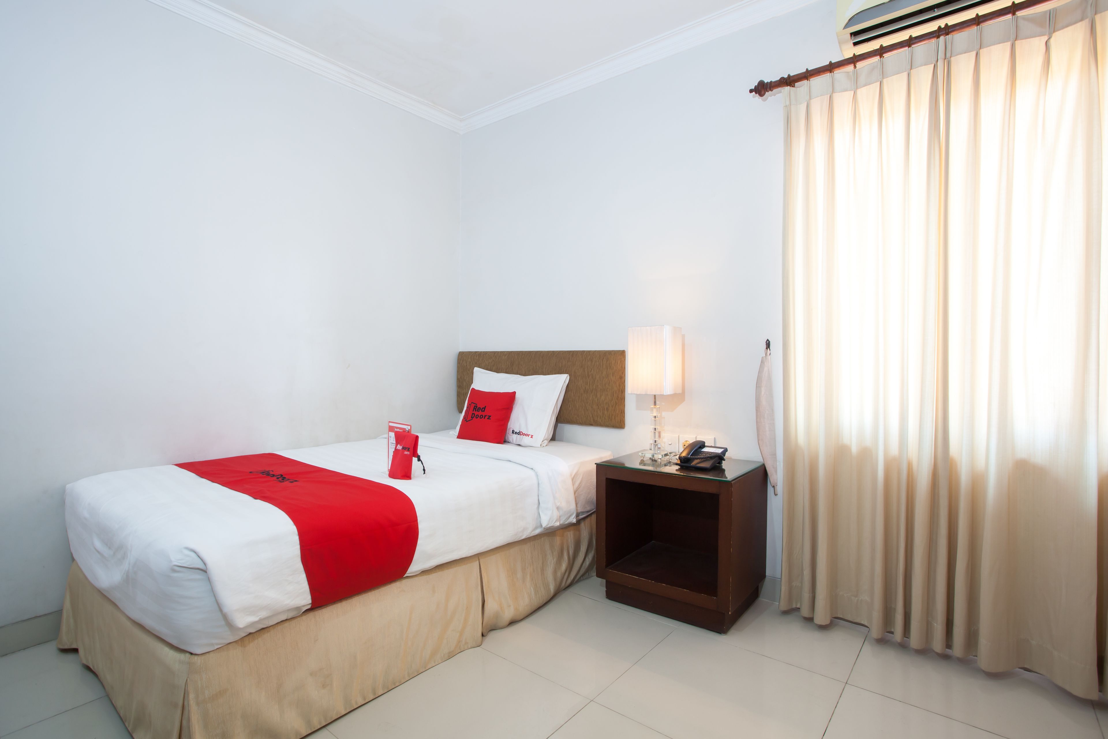 A hotel room with a bed, a nightstand, a lamp, and a window with curtains.