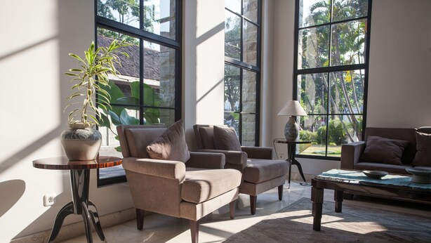 A spacious living room with large windows, a potted plant, and a coffee table. - RedDoorz Premium @ Raya Nginden (Surabaya)