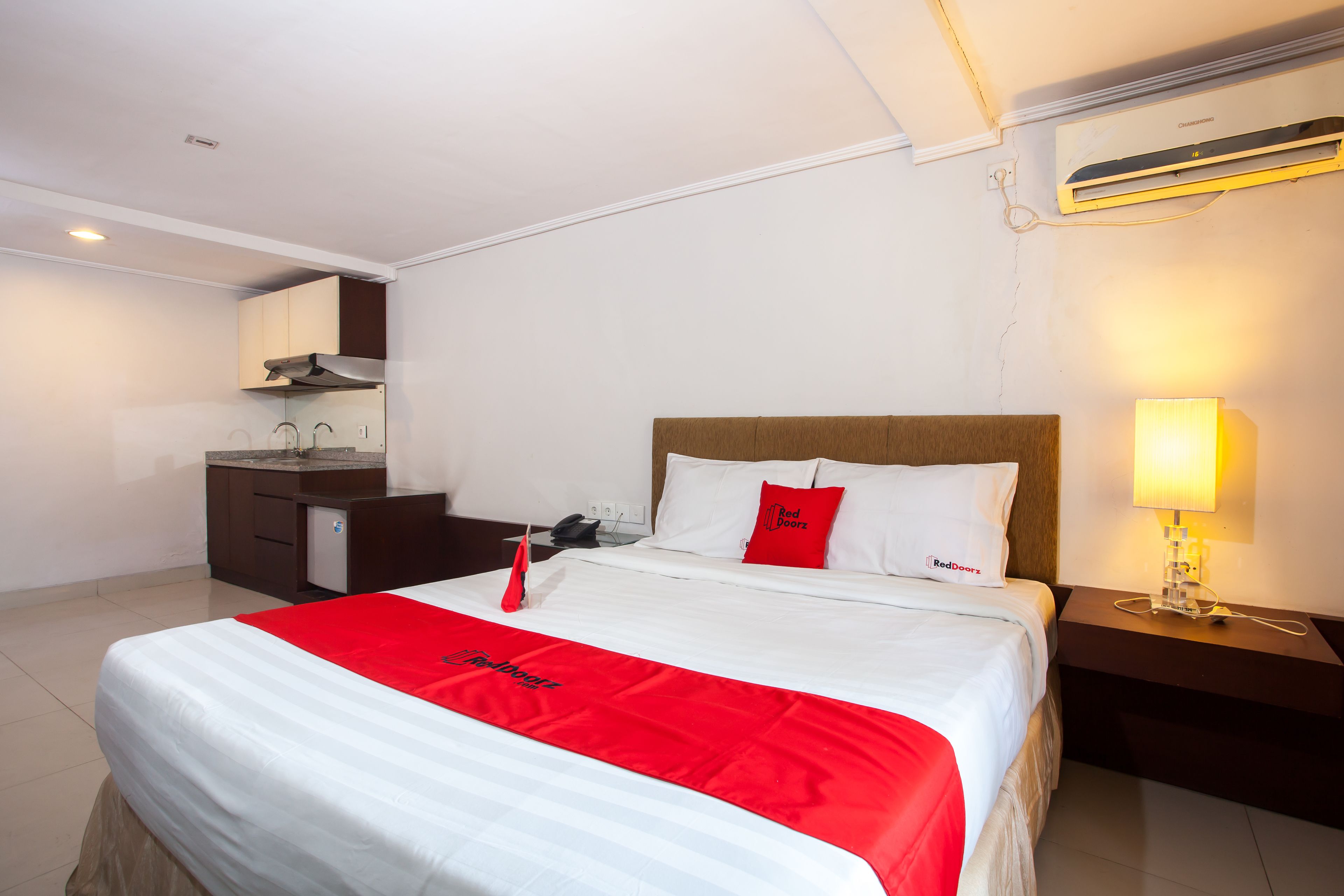 Hotelkamer met een bed, nachtkastje met lamp, klein bureau met telefoon en een kitchenette.