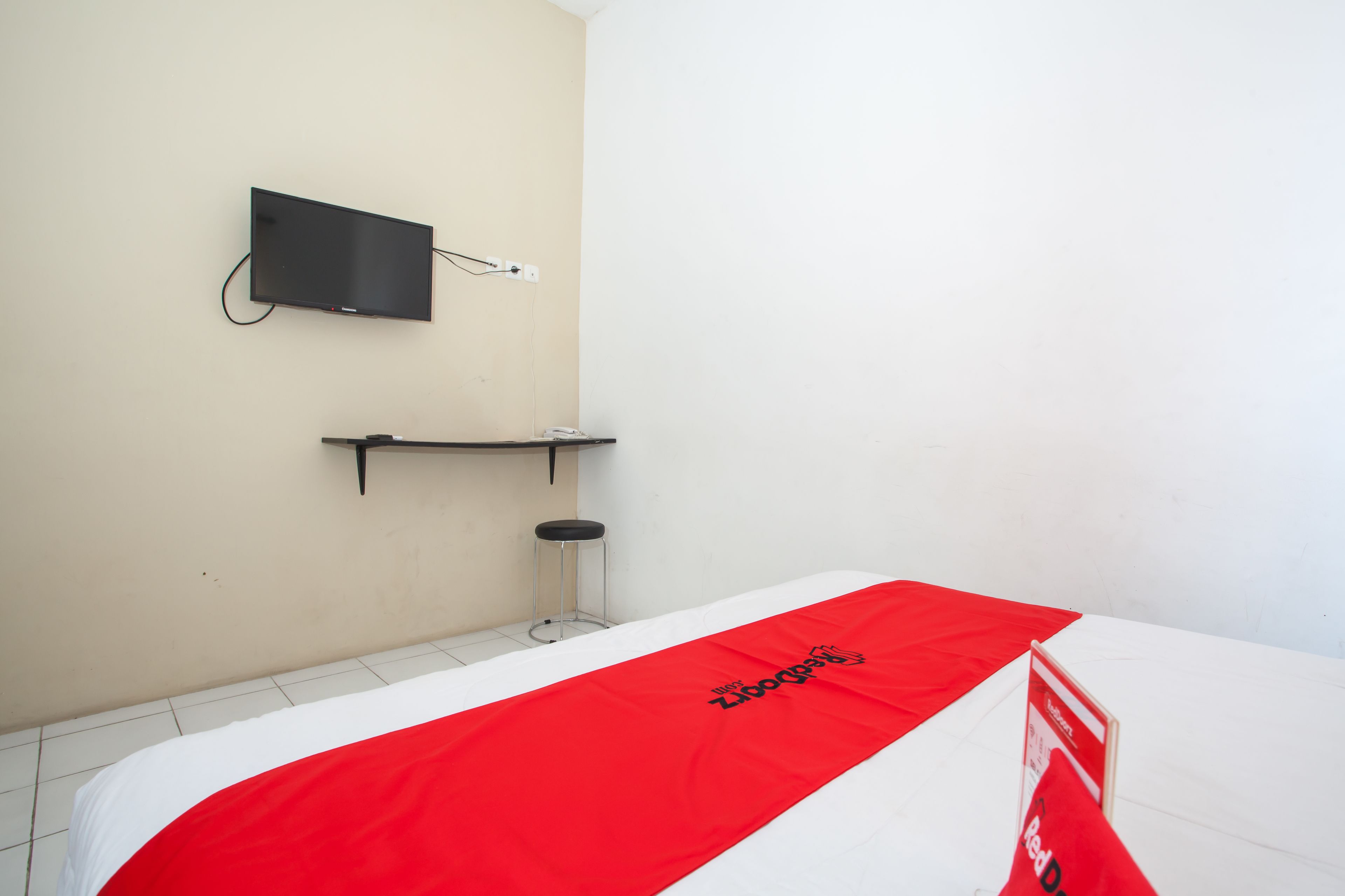 A hotel room with a bed, a television mounted on the wall, and a small stool.