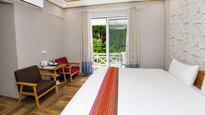 Une chambre d’hôtel avec un lit, un bureau, une chaise et une vue sur la verdure par la fenêtre.