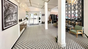 Un hall d’hôtel moderne avec un sol à motifs géométriques, une grande œuvre d’art encadrée, un lustre et un comptoir d’accueil.