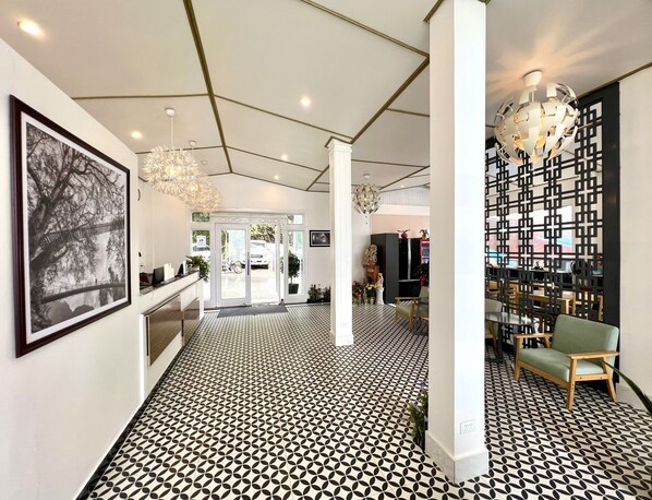 Eine moderne Hotellobby mit einem geometrisch gemusterten Boden, einem großen gerahmten Kunstwerk, einer Chandelüstere und einer Rezeption.