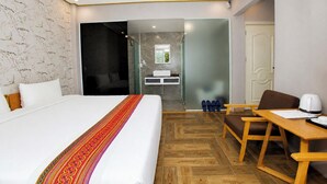 A hotel room with a bed, a desk, a chair, a bathroom with a mirror, and a shower.