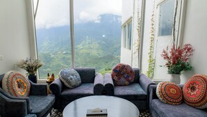 A room with a sofa set, a coffee table, and a view of a mountainous landscape through large windows.