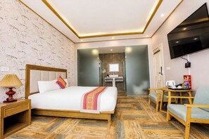Een hotelkamer met een bed, nachtkastje, lamp, televisie en een zithoek met een tafel en stoelen.