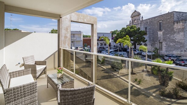 A balcony with wicker furniture and a view of a street with parked cars and a historic building. - La Casa del Cardinale (Monopoli)