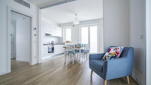 A modern kitchen with white cabinets, a dining table, and chairs. There is a blue sofa with a colorful pillow in the living area. - La Casa del Cardinale (Monopoli)