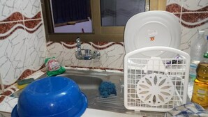 Una cucina con un lavandino, una ciotola blu, un espositore per piatti bianco e una bottiglia d'olio.