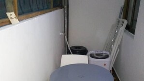 Un piccolo balcone chiuso con un tavolo rotondo e due sedie, una finestra con inferriata in metallo e un termosifone bianco.