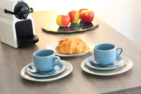 Una mesa con una cafetera, un croissant y dos tazas azules.