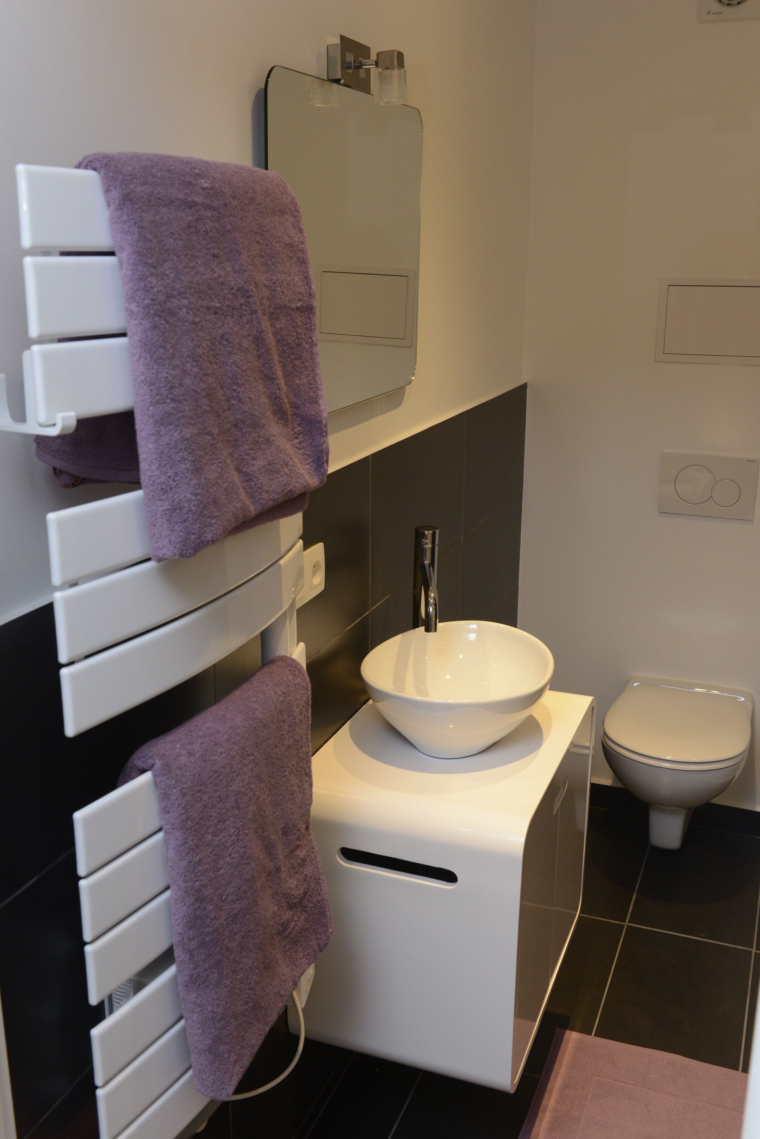 Une salle de bain moderne avec un lavabo blanc, des toilettes et un porte-serviettes orné de serviettes violettes.