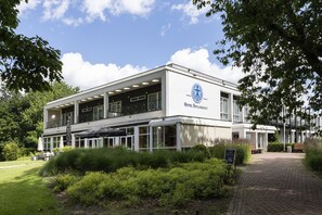 A modern hotel with a white facade, large windows, and a covered outdoor area with seating. - Hotel Spelderholt (Beekbergen)