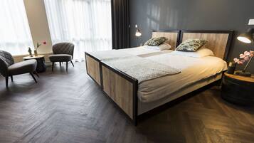 A modern hotel room with a large bed, two bedside tables, a chair, and a small table with a vase of flowers.
