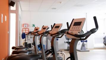 A row of stationary bikes in a gym with a white ceiling and orange walls.
