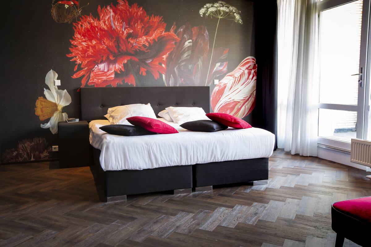 Una camera da letto moderna con un letto grande, una testiera scura e un murale floreale sulla parete.