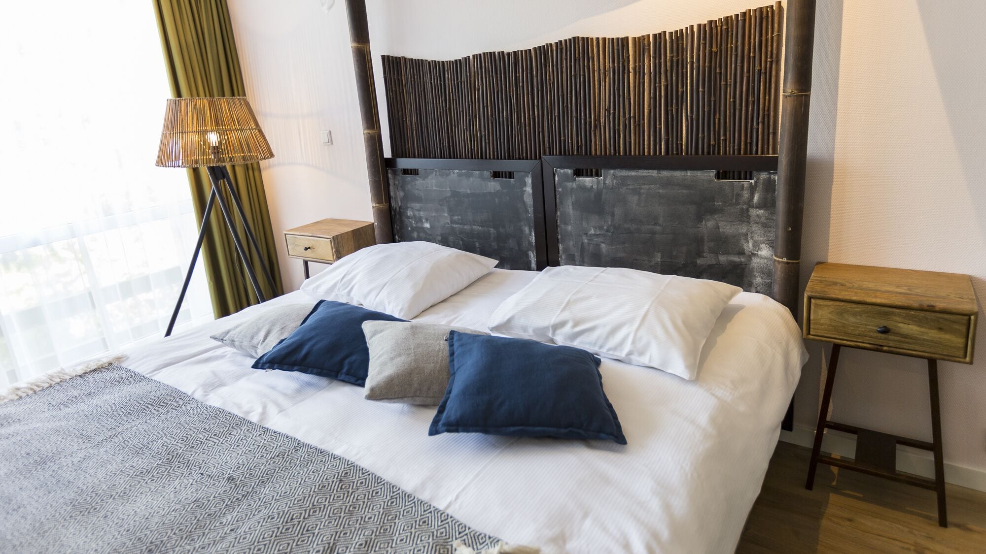 A modern hotel room with a large bed, two bedside tables, a lamp, and a view of the city.