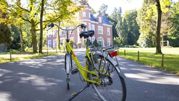 Ein gelbes Fahrrad steht auf einem gepflasterten Weg, im Hintergrund ist ein Gebäude mit roten Ziegeln zu sehen.