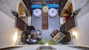 A narrow hallway with intricate tile work, a central seating area with cushions, and a hanging lantern. - Dar Settash (Fes)