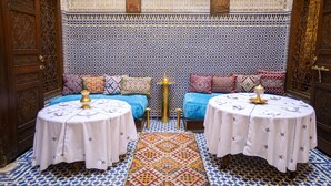 A traditional Moroccan room with two sofas, two round tables, and intricate tile patterns on the walls and floor. - Dar Settash (Fes)