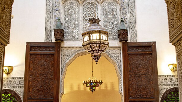 An ornate interior with a wooden door, a chandelier, and a sofa with cushions. - Dar Settash (Fes)
