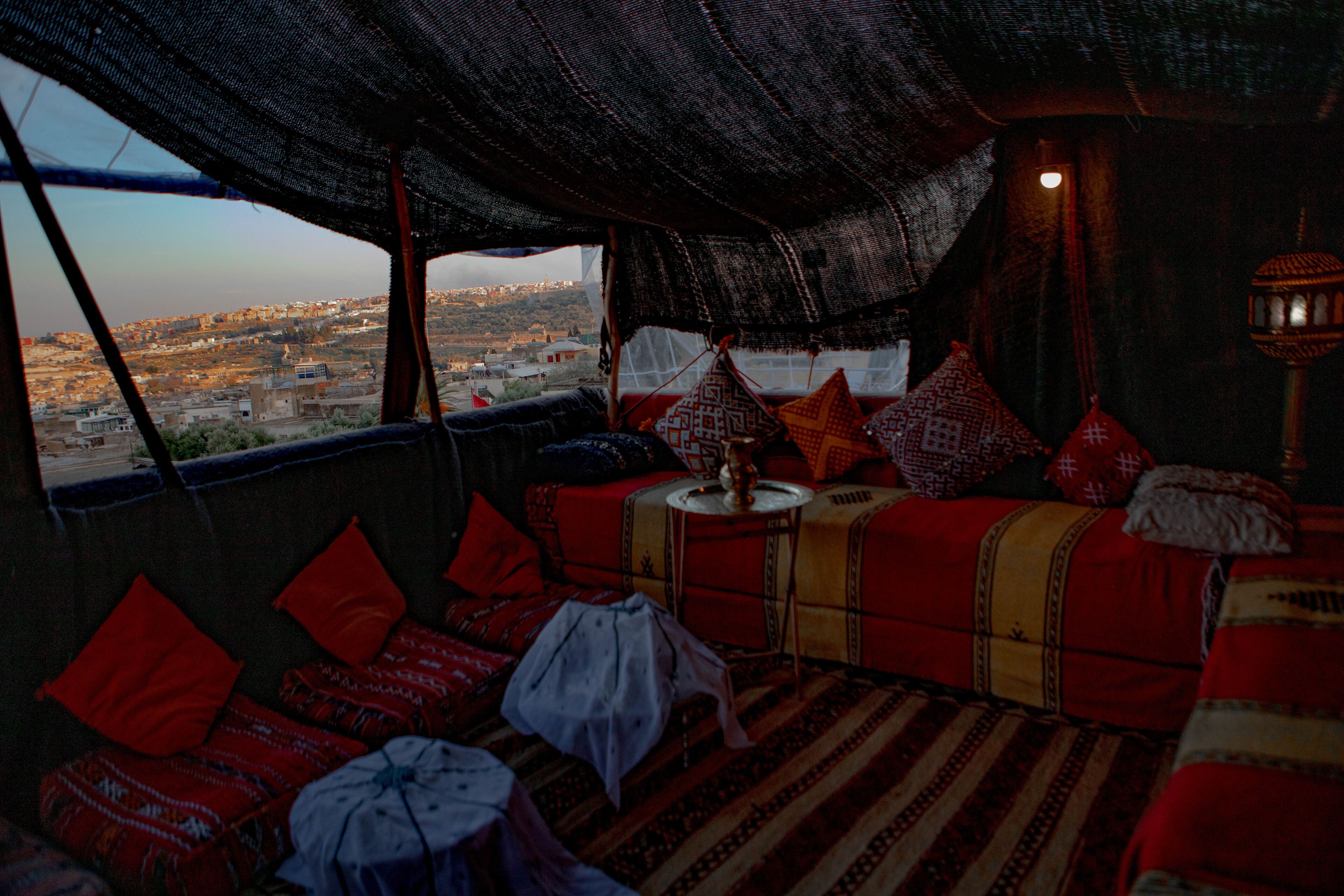 Acogedor cuarto con vista a la ciudad, que incluye un sofá estampado, cojines rojos y una pequeña mesa con un florero.
