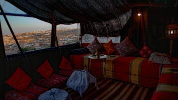 Acogedor cuarto con vista a la ciudad, que incluye un sofá estampado, cojines rojos y una pequeña mesa con un florero.